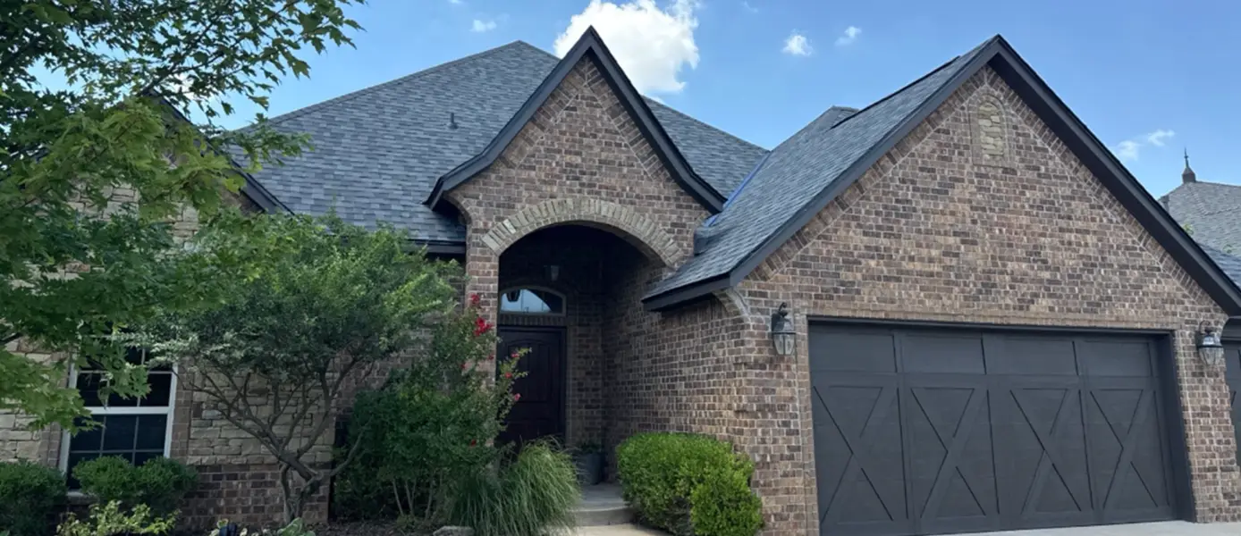 Brick suburban home with arched entry, dark front door, and a two-car garage with gray doors and landscaping in front.
