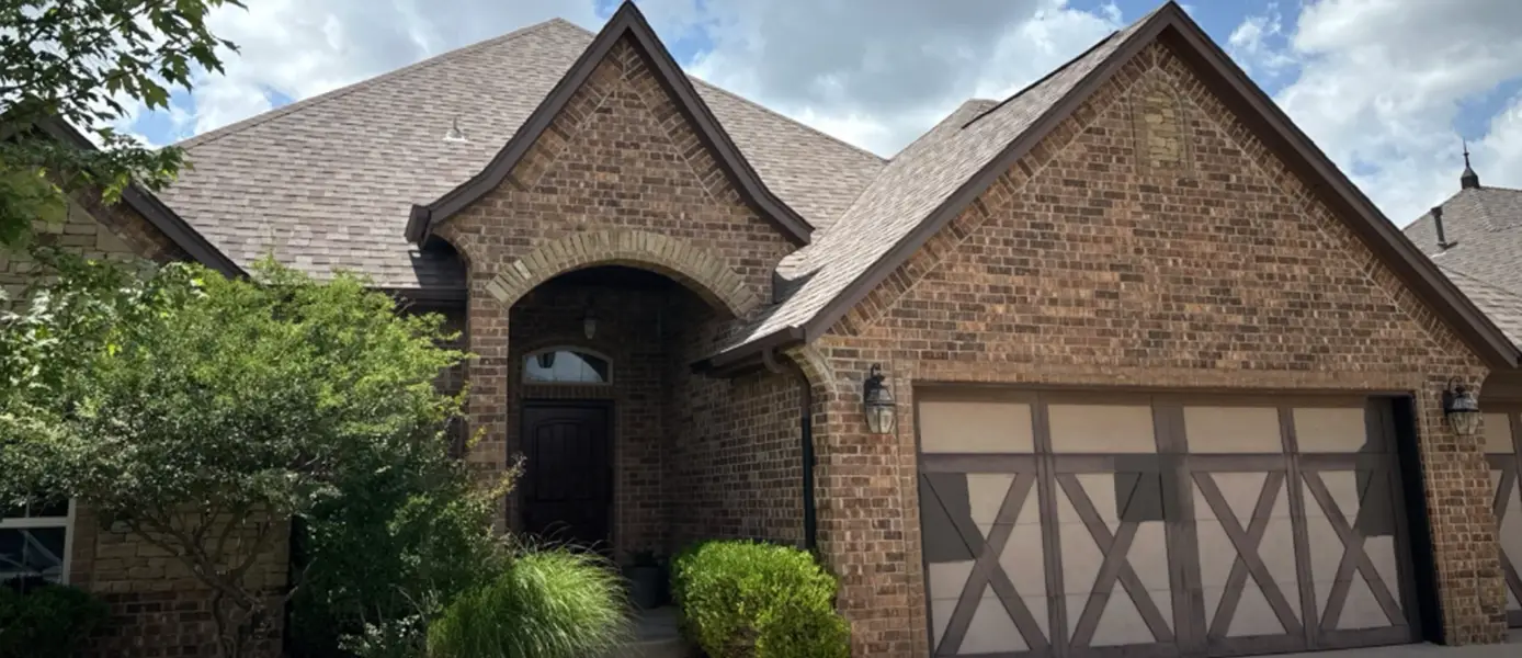Brick suburban home with an arched entry and a two-car garage, landscaped front yard under a blue sky.