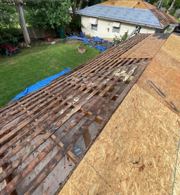 Roofer's wooden roof decking exposed with plywood sheathing, blue tarps and construction debris in the backyard during renovation.